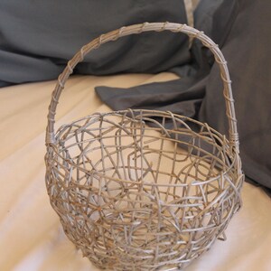 May include: A silver-colored wire basket with a handle. The basket has a rounded shape and is made of interwoven metal wires. The handle is also made of wire and is attached to the top of the basket.