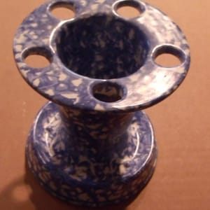 May include: A blue and white ceramic toothbrush holder with five holes for toothbrushes. The holder has a speckled blue and white glaze.