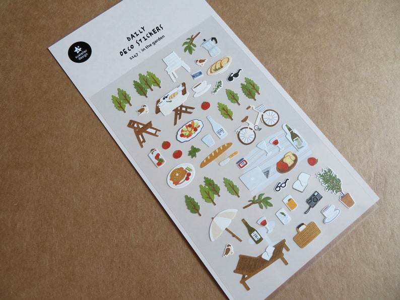 K&ouml;nnte beinhalten: Bogen mit dekorativen Aufklebern zum Thema Picknick. Enth&auml;lt Bilder von Essen, einem Fahrrad, einer Picknickdecke und den Texten "DAILY DECO STICKERS" und "in the garden". Die Aufkleber sind in verschiedenen Farben gehalten.