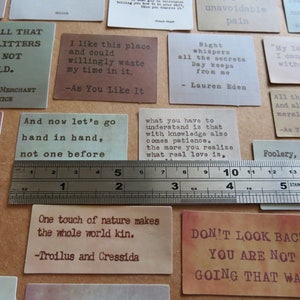 May include: A collection of rectangular cards with quotes in a variety of colors, including green, brown, and pink. A metal ruler measures the cards, which feature quotes from Shakespeare and other authors. The cards are approximately 2 inches wide.