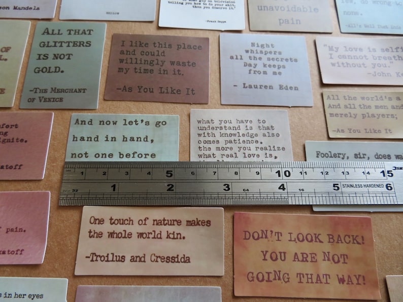 May include: A collection of rectangular cards with quotes in a variety of colors, including green, brown, and pink. A metal ruler measures the cards, which feature quotes from Shakespeare and other authors. The cards are approximately 2 inches wide.