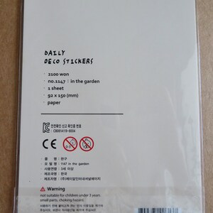 K&ouml;nnte beinhalten: Wei&szlig;e Verpackung von "DAILY DECO STICKERS" mit Text wie "no.1147: in the garden", Abmessungen von 92 x 150 mm und einem Warnhinweis zu Kleinteilen. Die Verpackung hat auch ein CE-Zeichen.