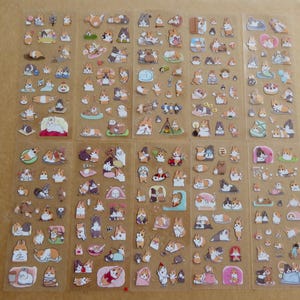 May include: Sheets of clear stickers featuring various cartoon corgi dog illustrations. The stickers depict corgis in different poses and activities, including sleeping, eating, and playing. The stickers are in shades of brown, white, and tan.