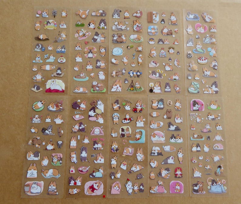 May include: Sheets of clear stickers featuring various cartoon corgi dog illustrations. The stickers depict corgis in different poses and activities, including sleeping, eating, and playing. The stickers are in shades of brown, white, and tan.