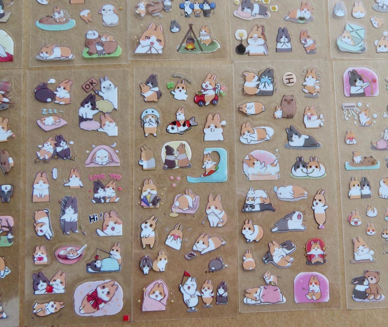 May include: Sheets of clear stickers featuring various cartoon rabbits in different poses and settings. The stickers showcase rabbits in various colors, including brown, white, and gray, with some stickers including text such as "OK" and "Hi!"