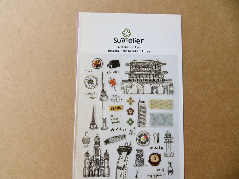 May include: A sheet of Suatelier stickers featuring illustrations of Korean landmarks and food. The stickers include drawings of a tower, a gate, food items, and the text "SEOUL". The sheet is labeled "no.1062: the beauty of korea".