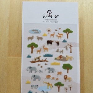 Puede incluir: Hoja de pegatinas Suatelier con animales y paisajes africanos. Incluye elefantes, leones, jirafas y árboles. Las pegatinas son de estilo caricatura, con fondo blanco y el texto "Suatelier" y "serengeti".