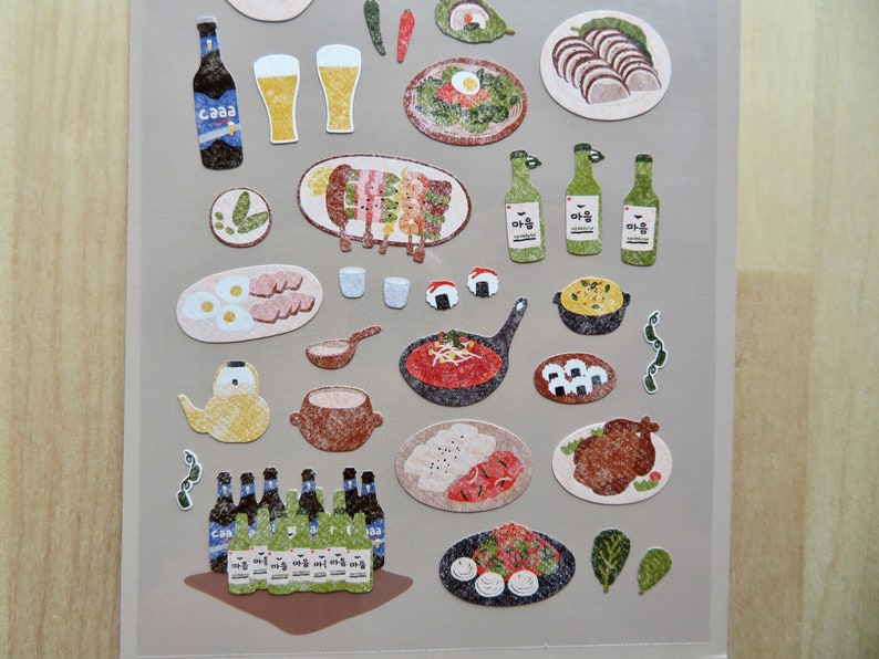 May include: A sheet of stickers featuring various Korean food illustrations. Includes images of beer bottles, glasses of beer, grilled skewers, eggs, sushi, and other dishes. The stickers have a textured, hand-drawn appearance.