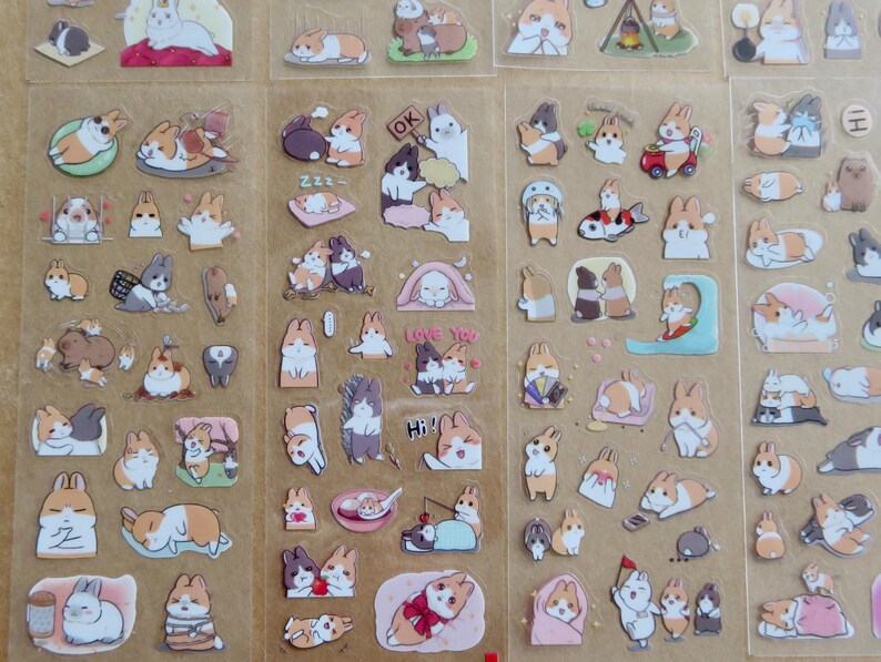 May include: Sheets of clear stickers featuring various cartoon rabbits in different poses and settings. The stickers showcase rabbits in various colors, including white, brown, and gray, with some wearing accessories or interacting with objects.