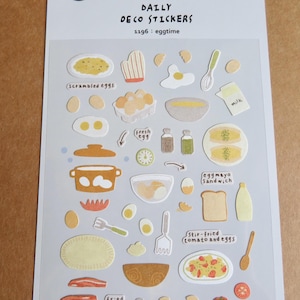 Puede incluir: Hoja de pegatinas decorativas con ilustraciones temáticas de desayuno. Incluye imágenes de huevos revueltos, huevos fritos, sándwich de huevo y tomate y huevos salteados. El texto "DAILY DECO STICKERS" y "1196: eggtime" son visibles.