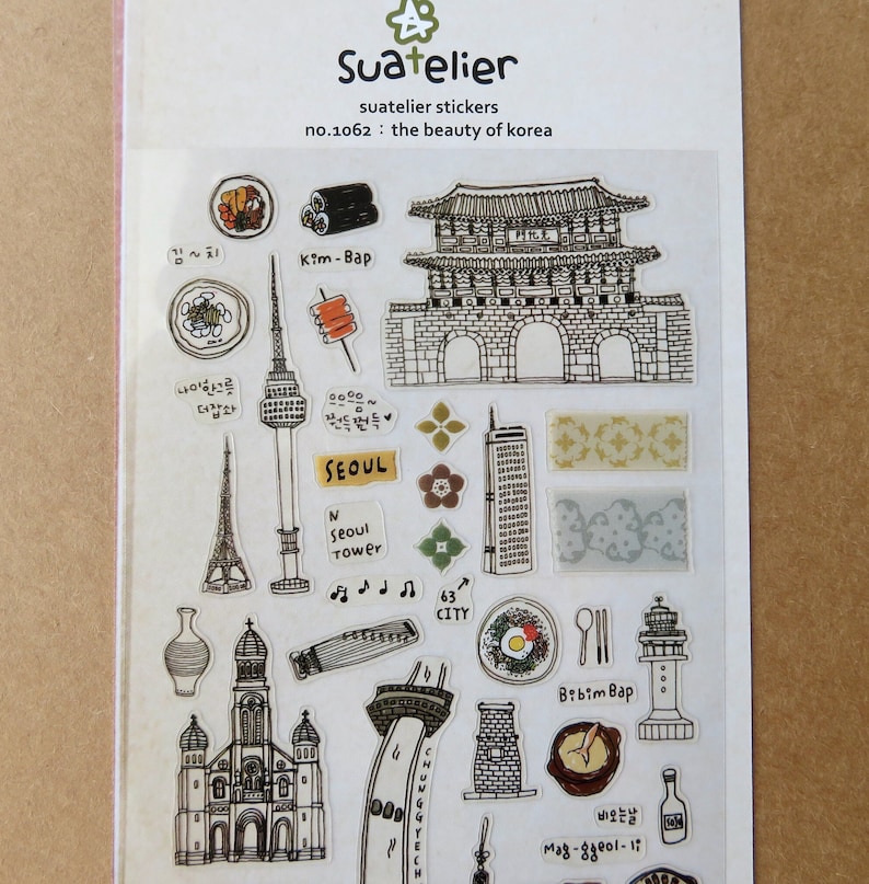 May include: Clear sticker sheet featuring various black and white illustrations of Korean landmarks and food. Includes images of a tower, gate, church, and dishes like Kim-Bap and Bibim Bap. The text "Suatelier" and "the beauty of korea" are also visible.