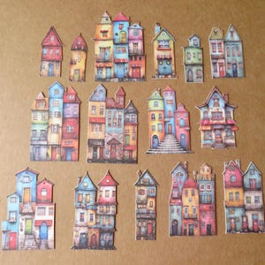 May include: A collection of colorful, paper cut-out houses in various architectural styles. Each house features unique details like doors, windows, and roof designs, with a palette of reds, blues, greens, and yellows. The houses are arranged on a neutral background.