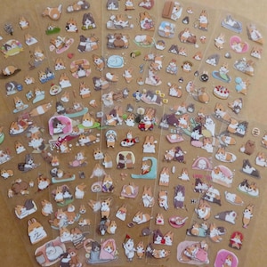 May include: Sheets of clear stickers featuring various cartoon corgi dog illustrations. The stickers depict corgis in different poses and settings, including sleeping, playing, and wearing outfits. The stickers are in shades of brown, white, and tan.