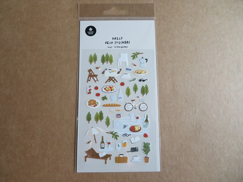 K&ouml;nnte beinhalten: Eine Packung dekorativer Aufkleber mit Gartenthema. Die Aufkleber zeigen Illustrationen von B&auml;umen, Essen, einem Fahrrad und Gartenm&ouml;beln. Der Text "DAILY DECO STICKERS" und "1147 in the garden" sind auf der Verpackung aufgedruckt.