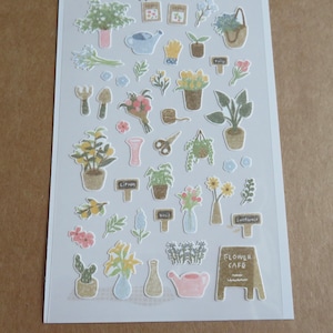 May include: A sheet of decorative stickers featuring various garden-themed illustrations. The stickers include potted plants, bouquets, gardening tools, watering cans, and signs. The stickers are in soft pastel colors, with the text "FLOWER CAFE" on one of the stickers.