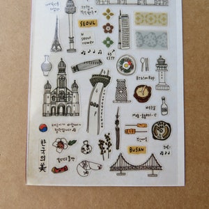 May include: A clear sticker sheet featuring hand-drawn illustrations of Korean landmarks and food. Includes the Seoul Tower, a church, a bridge, and the text "SEOUL" and "BUSAN". Also features Korean text and musical notes.