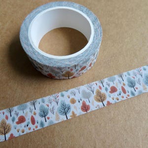 May include: A roll of decorative washi tape featuring a repeating pattern of stylized trees in shades of blue, orange, and yellow on a white background. The tape is partially unrolled, revealing the pattern. The tape roll is on a brown surface.
