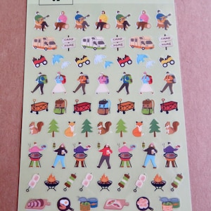May include: Sheet of camping-themed stickers featuring illustrations of campers, RVs, camp signs, binoculars, hikers, backpacks, wagons, squirrels, foxes, trees, grilling, skewers, and food items. The stickers are on a light green background.