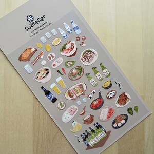 May include: A sheet of Suatelier stickers with food illustrations. The stickers depict sushi, beer, bottles, and other dishes. The text "Suatelier stickers no.1109 food trip #3" is printed on the top of the sheet.