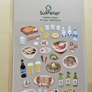 May include: A sheet of Suatelier stickers with illustrations of food items such as grilled meat, bowls of soup, sushi, and bottles of water and beer. The text "Suatelier stickers" and "Food trip #3" are visible.