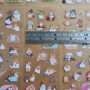 May include: Sheets of colorful bunny stickers with various poses and accessories. The stickers include bunnies with hats, fish, and text like "OK" and "Love You". A ruler shows the stickers are approximately 5 inches wide.