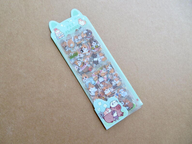 May include: A package of stickers featuring various cartoon animals, primarily dogs and rabbits, in a variety of poses and colors. The package is light green with the text "PET PLANET" and a cartoon illustration of animals.