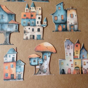 May include: A collection of whimsical, watercolor-style paper cutouts of colorful houses and mushroom-shaped structures. The houses feature various architectural styles and are painted in shades of blue, orange, and white. The overall theme is fantasy and fairytale.