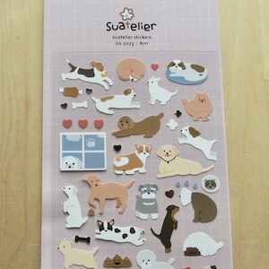 May include: Sheet of Suatelier stickers featuring various dog breeds in cartoon style. The stickers include dogs in different poses, along with hearts, bones, and a window with a dog looking out. The stickers are on a pink grid background.