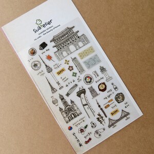 May include: A sheet of Suatelier stickers featuring black and white illustrations of Korean landmarks, food, and cultural symbols. The stickers include images of a tower, a bridge, and various food items, with text in Korean and English.