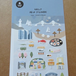May include: Sheet of "DAILY DECO STICKERS" featuring travel-themed illustrations. Includes images of a lighthouse, sailboats, bridge, buildings, food, and other Busan, South Korea landmarks. The text "1353: travel in Busan" is also present.