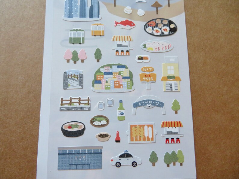 May include: A sheet of colorful stickers featuring various illustrations of buildings, food, and transportation. Includes images of a cityscape, a cable car, a taxi, and various food items. The stickers are in a cartoon style.
