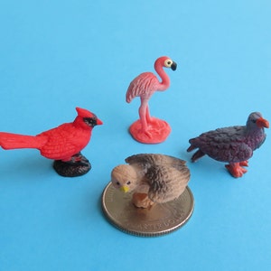 以下が含まれることがあります： 4つのミニチュア鳥の置物：赤いカーディナル、ピンクのフラミンゴ、茶色の鷹、紫色の鳥。 鷹は硬貨の上にいます。 鳥は単色の青い背景に配置されています。