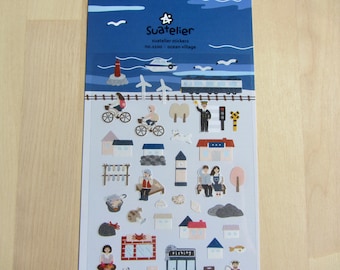 May include: Sheet of Suatelier stickers featuring an ocean village theme. The stickers include illustrations of a lighthouse, boat, train, bicycles, houses, people, and various seaside elements. The color palette is primarily blue, white, and earth tones.