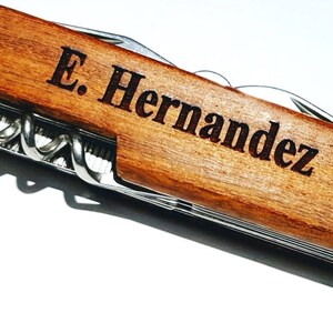 May include: A brown wooden pocket knife with a silver blade and multiple tools. The knife is engraved with the name "E. Hernandez".