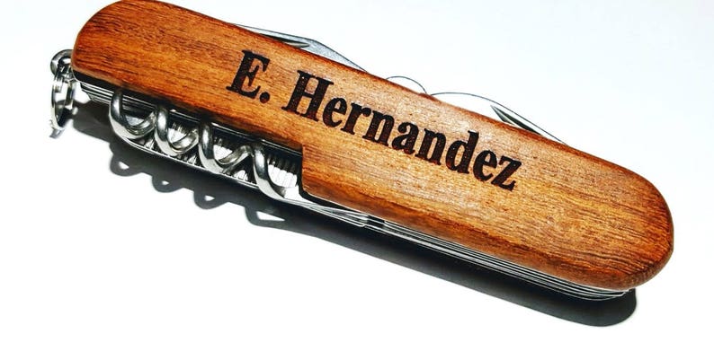 May include: A brown wooden pocket knife with a silver blade and multiple tools. The knife is engraved with the name "E. Hernandez".