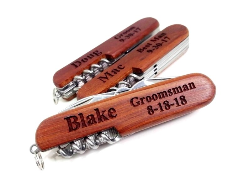 May include: Four wooden pocket knives with personalized engravings. The knives have a corkscrew, bottle opener, and other tools. The engravings include "Doug Groom 9-30-17", "Mac Best Man 9-30-17", "Blake", and "Groomsman 8-18-18".