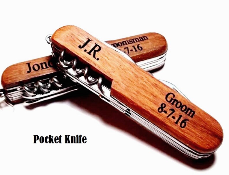 May include: Two wooden pocket knives with personalized engravings. The top knife has the text "J.R. groomsman 8-7-16" and the bottom knife has the text "Groom 8-7-16".