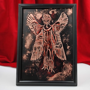 May include: A framed copper relief sculpture of a winged humanoid figure with a detailed, grotesque face. The figure is depicted with wings, claws, and a skeletal body. The background is black with a copper patina.
