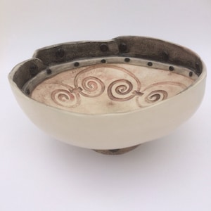 May include: A white ceramic bowl with a brown rim and black accents. The bowl has a textured design with a series of spirals on the inside.