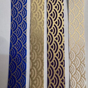 May include: Four decorative ribbons with a repeating wave pattern. The ribbons are in shades of blue, beige, purple, and white, each with a gold metallic design. The ribbons are ideal for crafting and embellishments.
