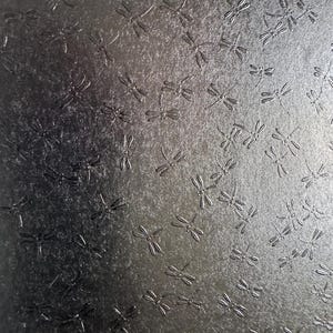 May include: A black textured background with a repeating pattern of silver dragonfly shapes.