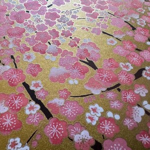 May include: A close-up of a gold background with a pattern of pink and white cherry blossoms. The blossoms are painted in a delicate style, with a hint of sparkle.