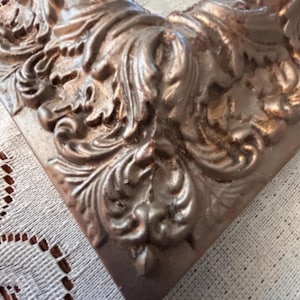 May include: A corner section of a rectangular picture frame featuring a metallic bronze finish with an ornate, raised relief pattern of scrolling acanthus leaves and floral motifs. The frame has a deep, dimensional profile with dark highlights.
