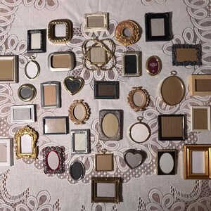 May include: A collection of numerous miniature picture frames in various shapes, including rectangular, oval, heart, and circular designs. The frames feature diverse finishes such as gold, silver, black, and wood tones, with some displaying ornate detailing.