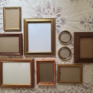 May include: A collection of various picture frames in different shapes and sizes. The frames are made of wood and metal, with gold, brown, and bronze finishes. Some frames have glass, while others are empty.