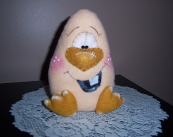 May include: A beige felt toy shaped like an egg with a brown felt beak, a black felt mouth, and a white felt eye. The toy has two brown felt feet.