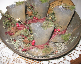 May include: Three vintage-style fabric top hats decorated with red berries, sprigs of greenery, and rusty stars. The hats are arranged in a metal bowl with a brown, rustic finish. The bowl is filled with dried grass and the text "Into the Woods..." is visible on a small sign.