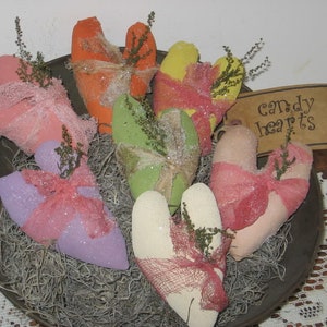 May include: A bowl filled with handmade fabric hearts in various colors, including pink, purple, green, yellow, and orange. The hearts are decorated with lace, ribbons, and glitter. The bowl is sitting on a white lace doily. A sign reads "candy hearts".