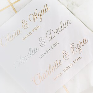 May include: White paper with gold, silver, and rose gold foil lettering. Names include Olivia & Wyatt, Amelia & Declan, and Charlotte & Ezra. The words "GOLD FOIL", "SILVER FOIL", and "ROSE GOLD FOIL" are also printed on the paper.