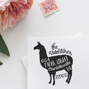 May include: Black silhouette of a llama with white text overlayed on the body. The text reads "the valentines 654 paper street charlottesville VA 22702".